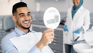 Man with white teeth smiling at reflection in dentist's mirror