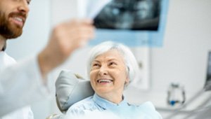 Senior woman smiling at emergency dentist holding X-ray