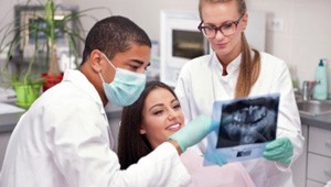 Dentist and dental assistant reviewing X-ray with smiling patient